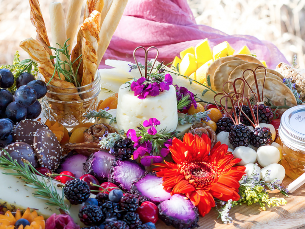 The cheese board pictured is beautifully styled with fresh flowers. Courtesy: Picnic + Petal